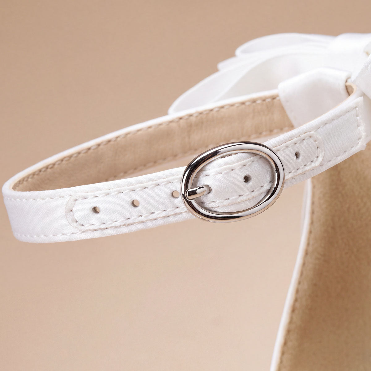 Close-up of the round metal buckle and adjustable ankle strap on a white satin pump