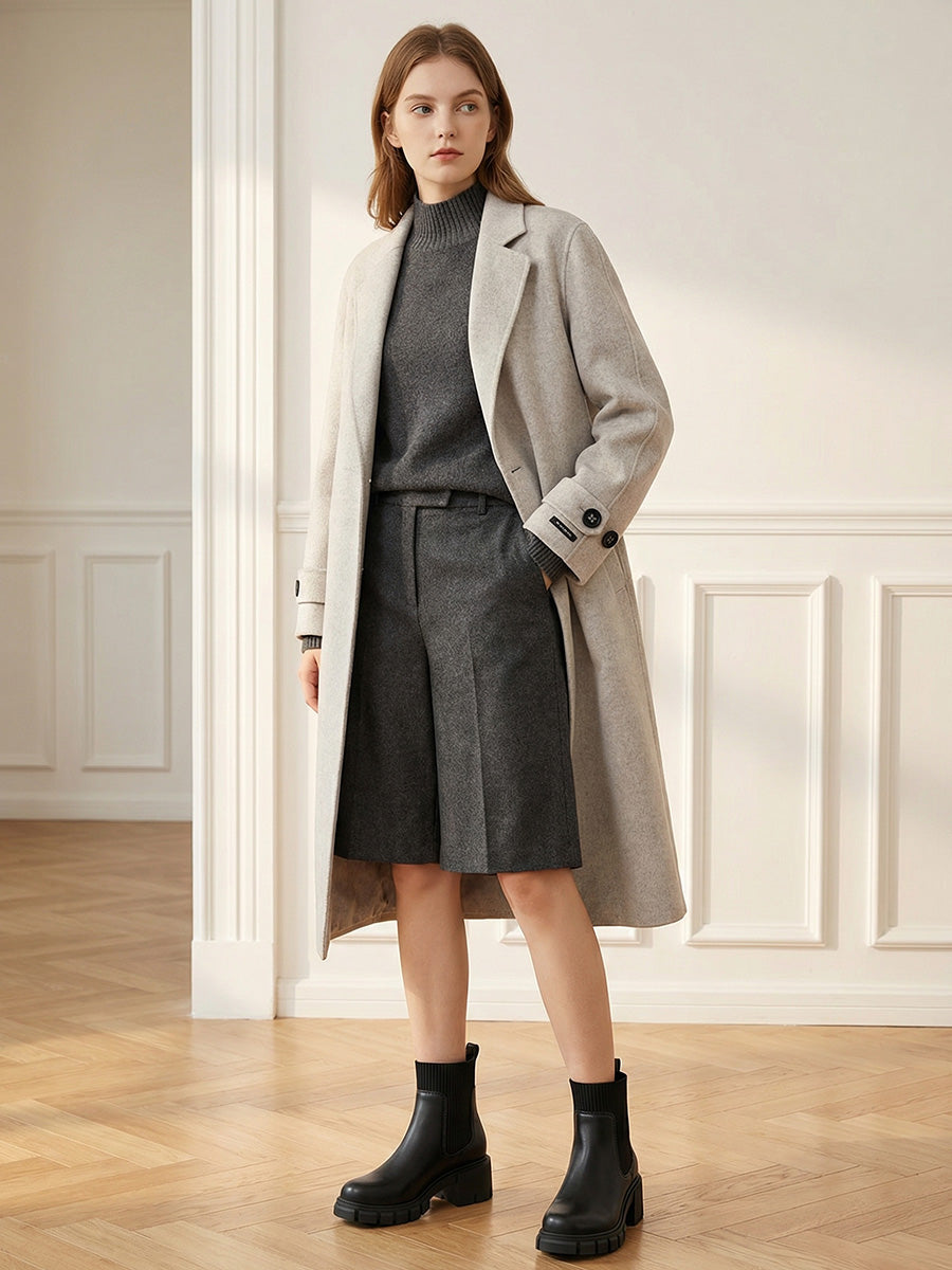 Black Chelsea boots styled with a charcoal skirt and a light gray coat