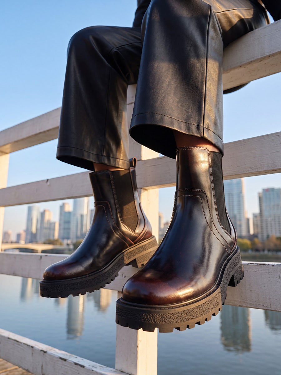 Black chunky Chelsea boots styled with cropped black leather-look trousers while seated on a waterfront railing