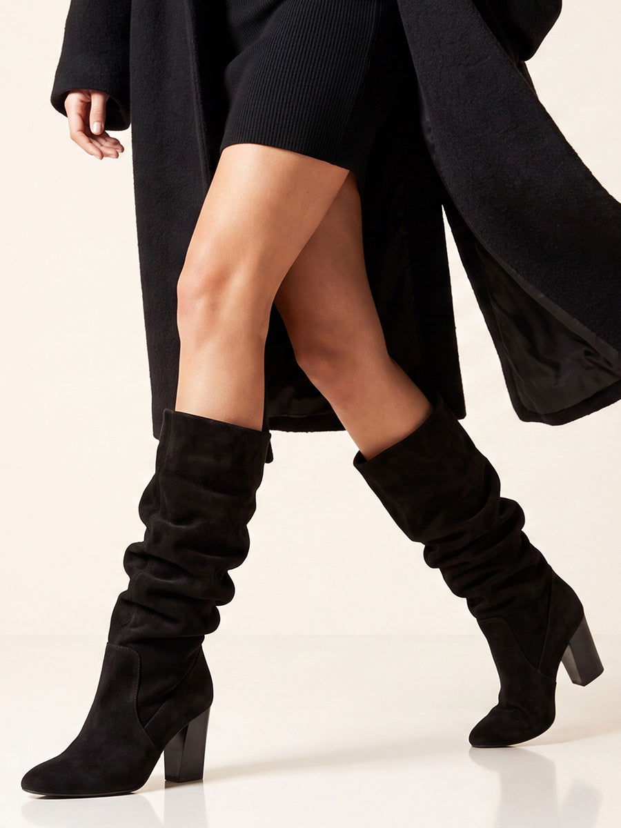 Black suede boots worn with slouched shafts, styled with a black mini skirt and long coat