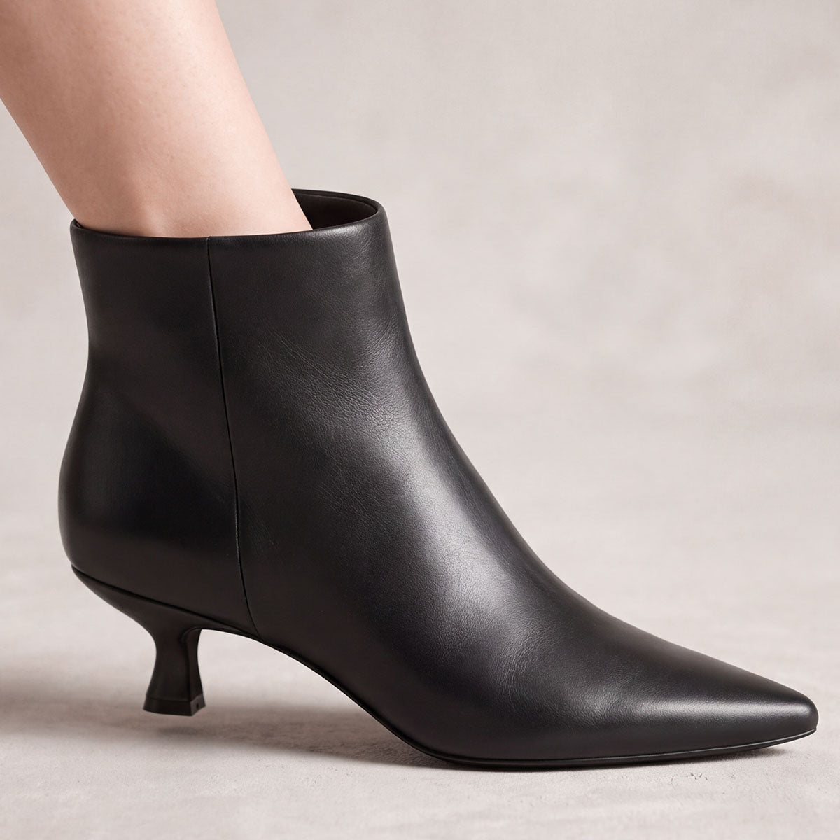 Side view of a black kitten-heel ankle boot showing the ankle shaft and pointed toe