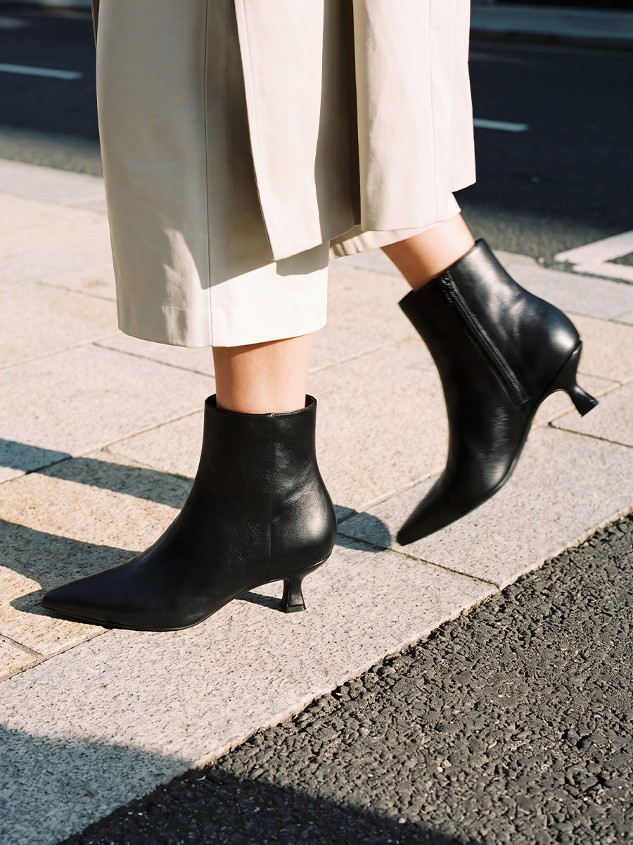 Close-up of black pointed-toe kitten-heel ankle boots worn with cropped beige trousers