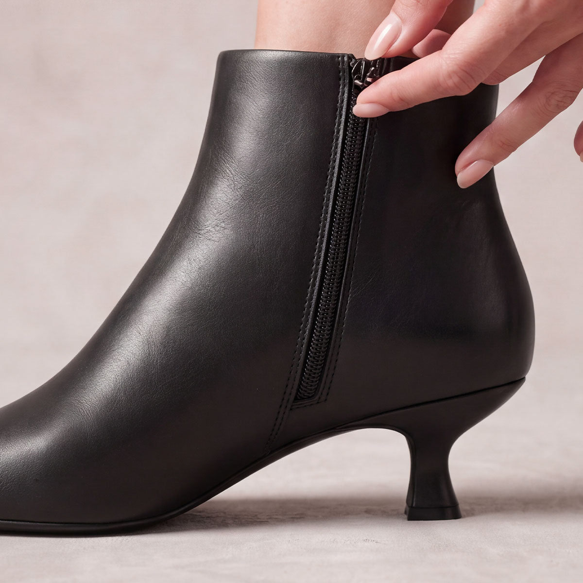 Close-up of the side zipper being opened on a black kitten-heel ankle boot