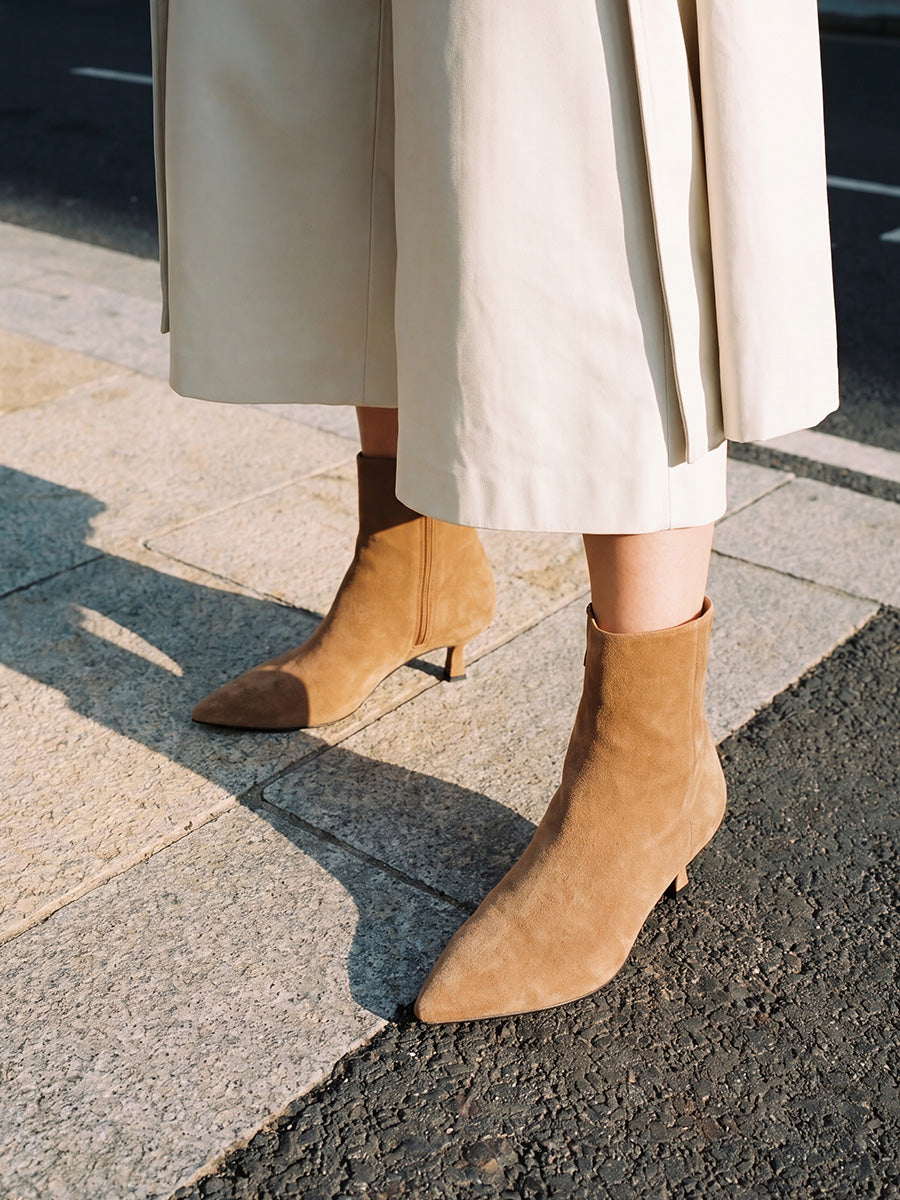 Close-up of brown suede pointed-toe kitten-heel ankle boots styled with a cream midi skirt