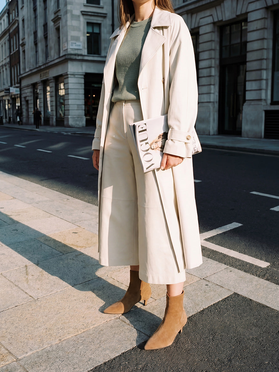 Model wearing brown suede kitten-heel ankle boots with a cream midi skirt, green top and light trench coat