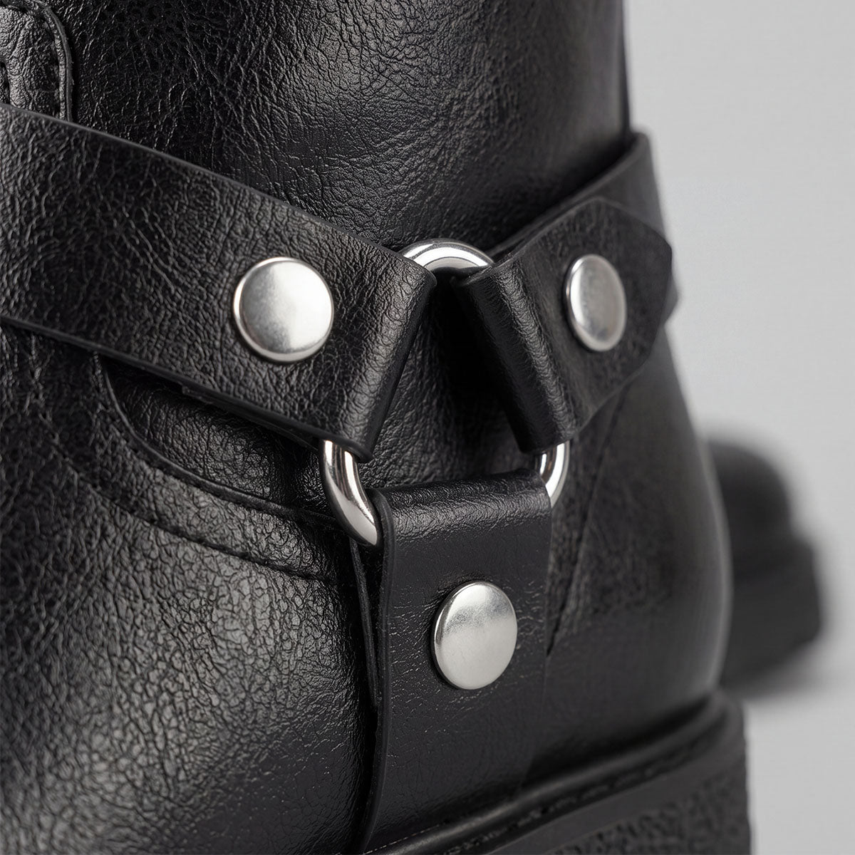 Close-up of the metal ring, harness straps and silver rivets on a black moto boot