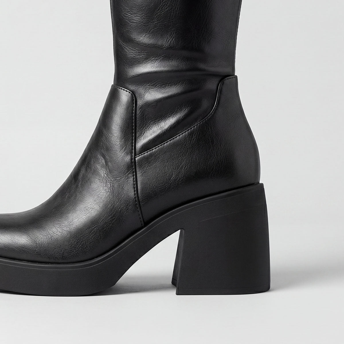 Side view of the chunky block heel and platform sole on a black knee-high boot