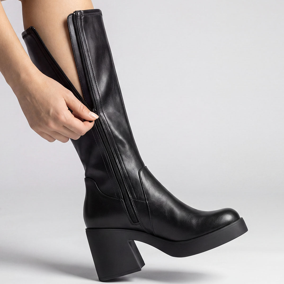 Close-up of the side zipper being opened on a black platform knee-high boot