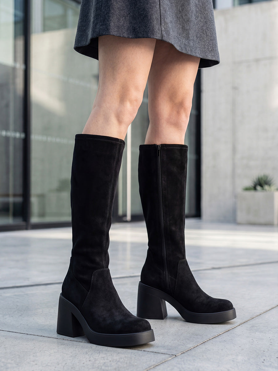 Black suede platform knee-high boots with chunky block heels styled with a charcoal mini skirt