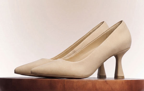 Side view of nude pointed-toe pumps with flared heels displayed on a wooden surface