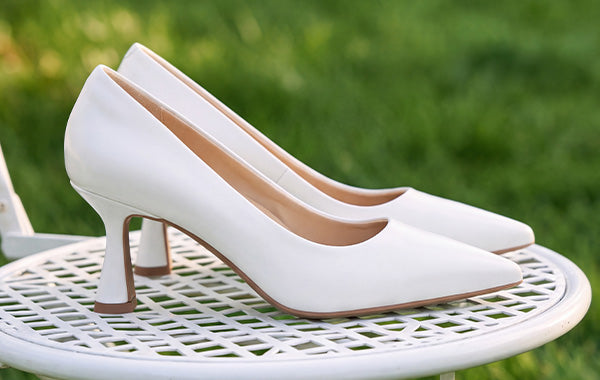 White pointed-toe pumps with flared heels displayed on a white garden table