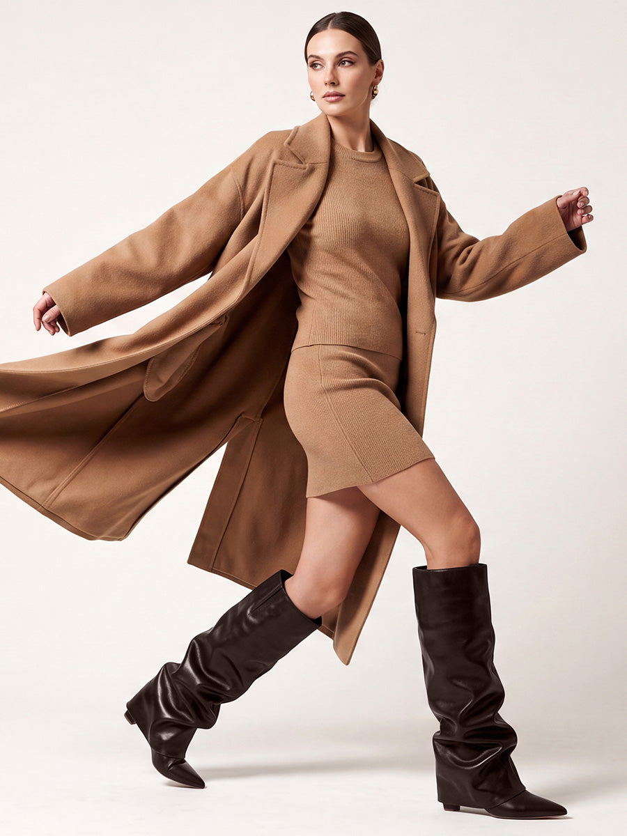 Model wearing brown slouchy pointed-toe boots with a tan mini dress and a long brown coat