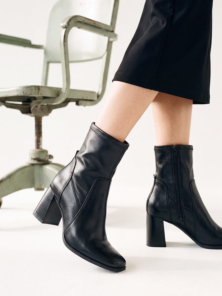 Close-up of black square-toe ankle boots with block heels, worn with a black dress